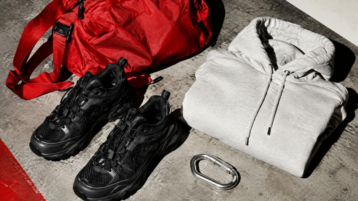 A red nylon bag, black runners, a gray hoodie and a carabiner on concrete