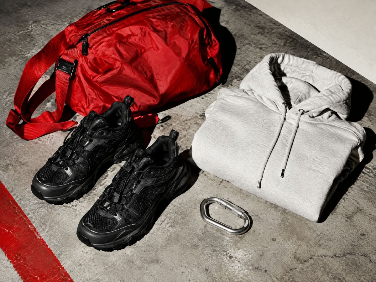 A red nylon bag, black runners, a gray hoodie and a carabiner on concrete