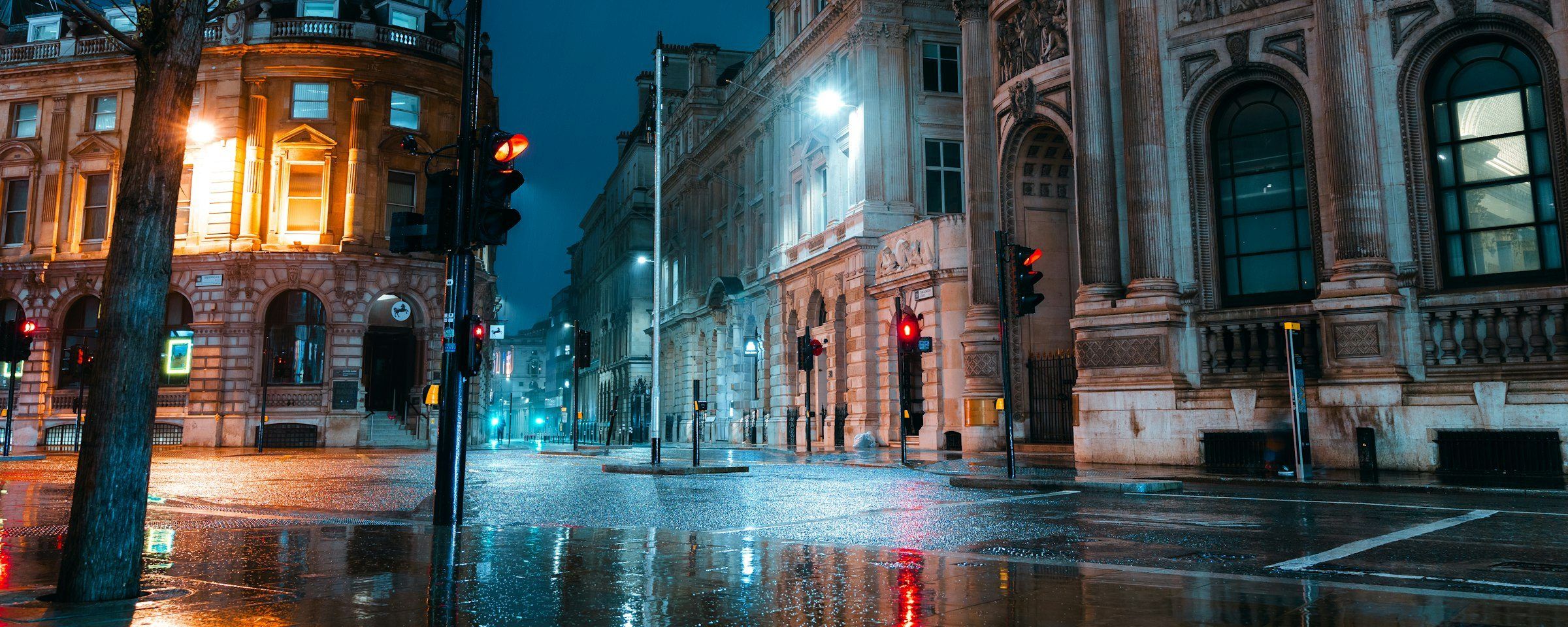 A wet city street at night, lit shopfronts and a red traffic light